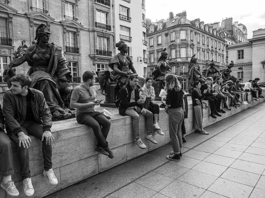 Black and white photo of people relaxing near statues in Paris.