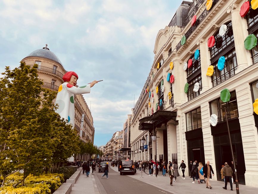 Vibrant Paris street with colorful building decorations and giant sculpture, capturing urban life and art.