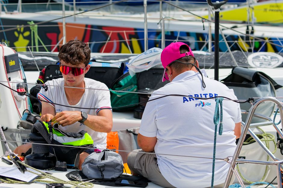Crew members prepare equipment on a sailboat during a sunny day at the marina.
