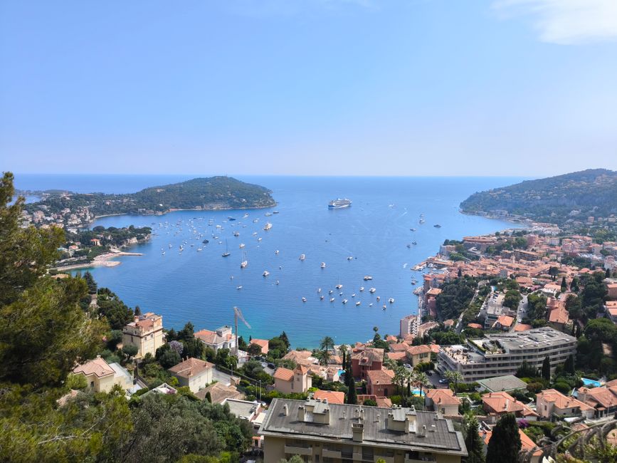 A breathtaking aerial view of Villefranche-sur-Mer with numerous boats and a cruise ship in a serene bay.