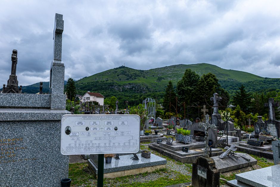 Peaceful cemetery scene with gravestones and mountain view under cloudy sky.