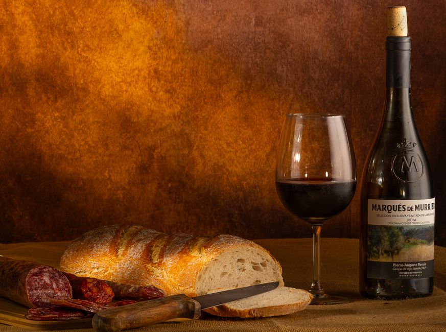 A rustic still life of wine, bread, and charcuterie in a warm setting.