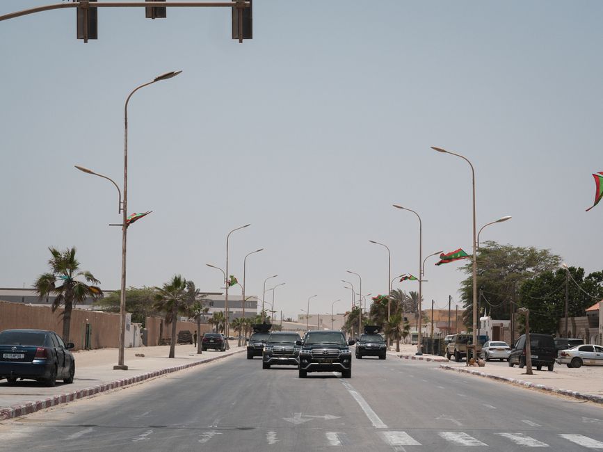 A street in Mauritania with cars and national flags under a clear sky.
