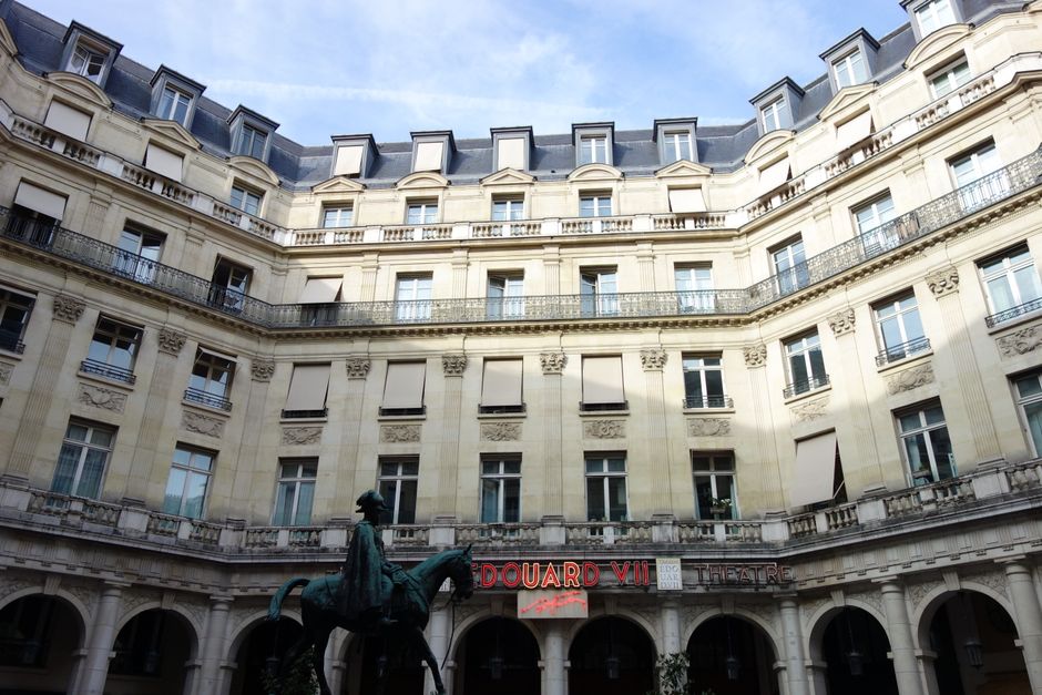 Elegant architecture of Edouard VII Theatre courtyard in Paris with a statue at the center.