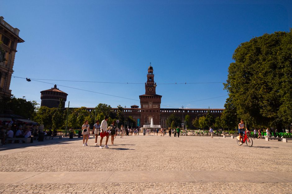People enjoying a sunny day at Sforza Castle in Milan, Italy, a historical landmark with vibrant surroundings.