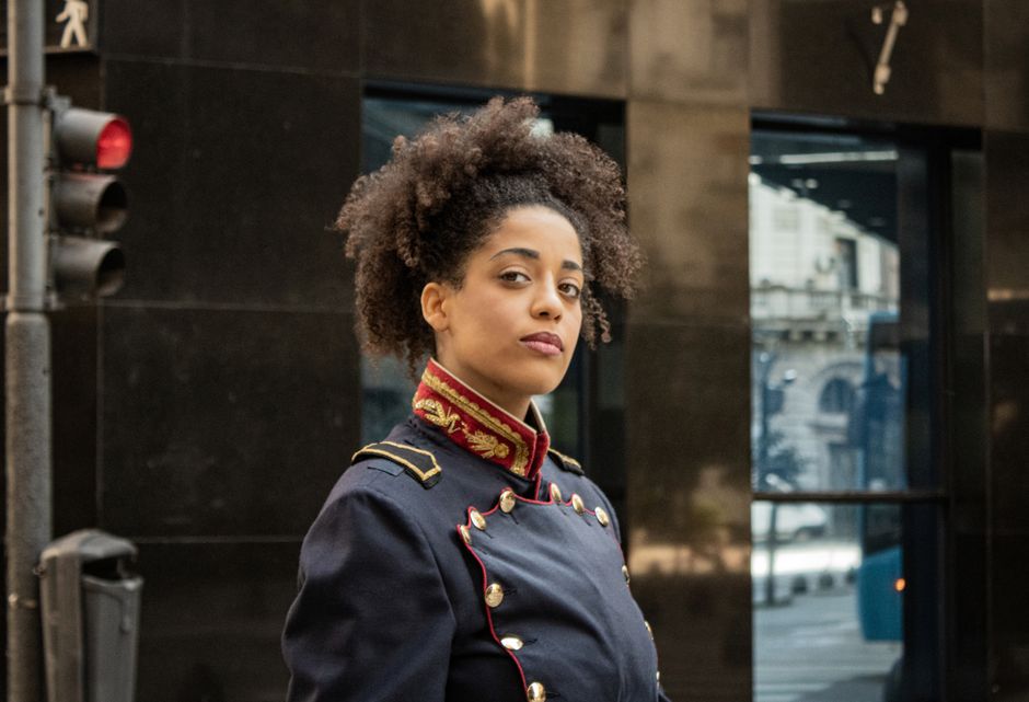 Portrait of a confident woman wearing a military-style jacket on a city street.