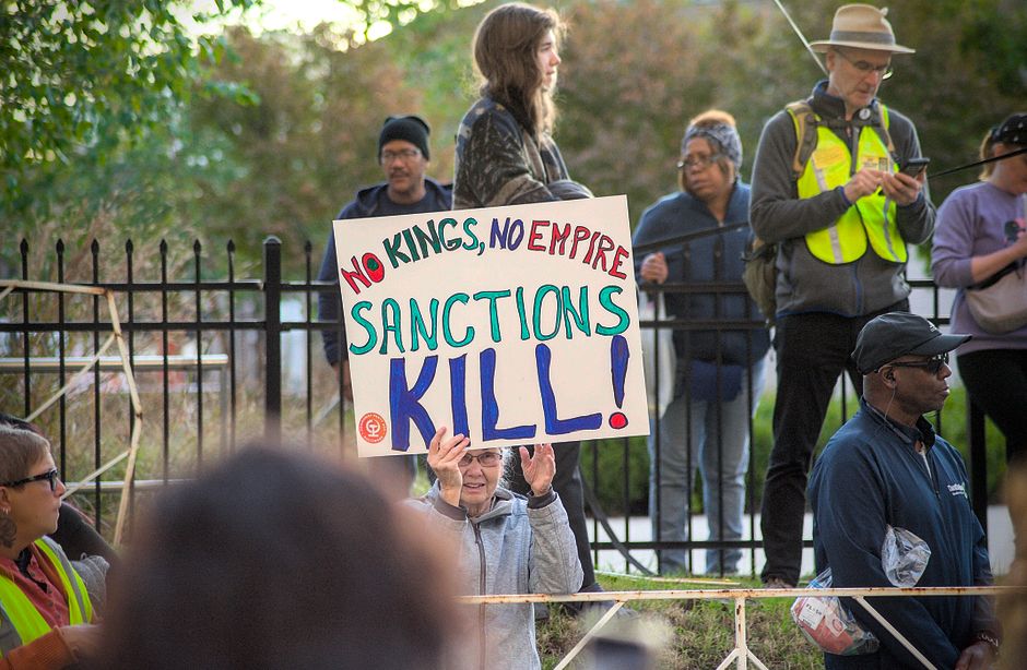 Protesters gather in Towson with signs against sanctions, advocating for peace and justice.