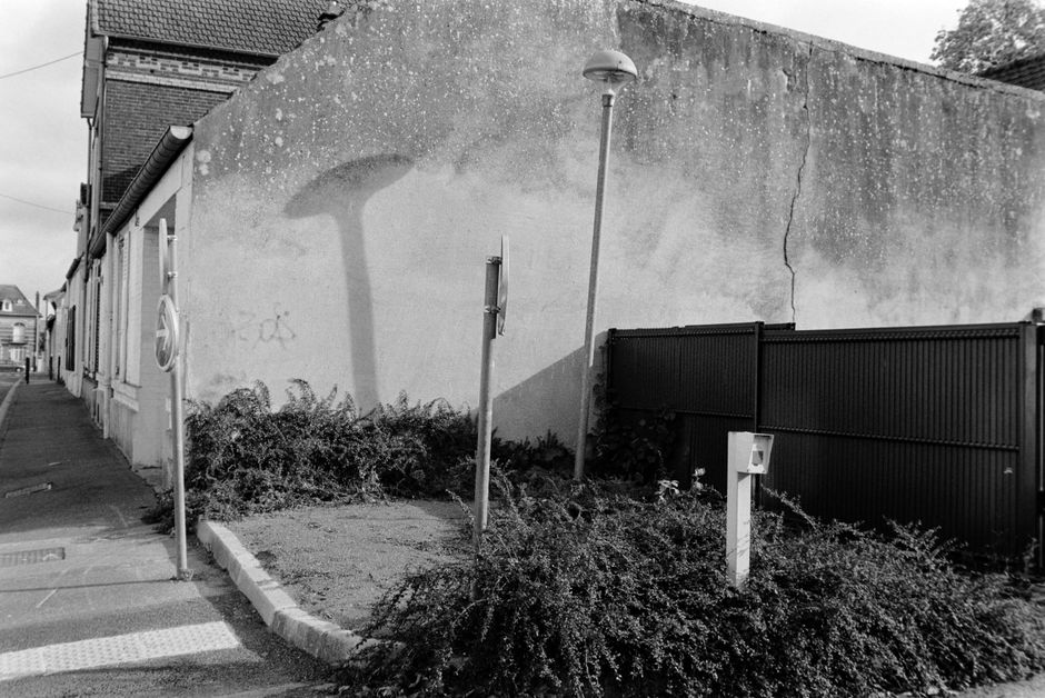 Street scene in Compiègne, France features a wall, lamppost, and overgrown plants in black and white.