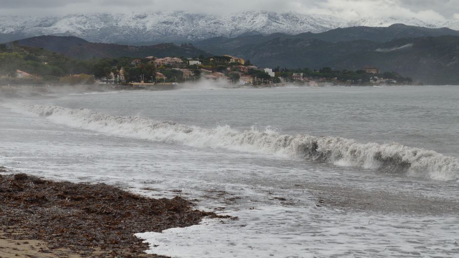 Captivating view of Saint-Florent beach with mist over the sea and snow-capped mountains.