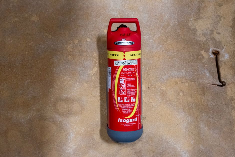 Red Isogard fire extinguisher mounted on a textured wall, focused view.