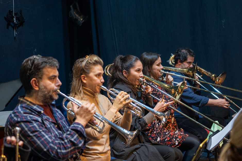 Musicians from an orchestra brass section performing on stage during a rehearsal.