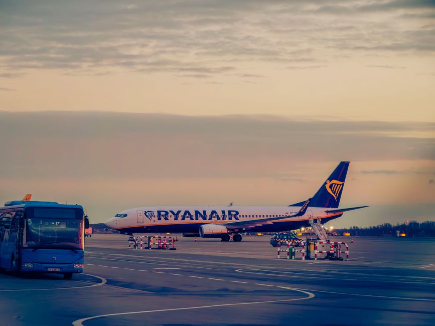 Ryanair aircraft and bus at Wrocław Airport's tarmac during sunset.