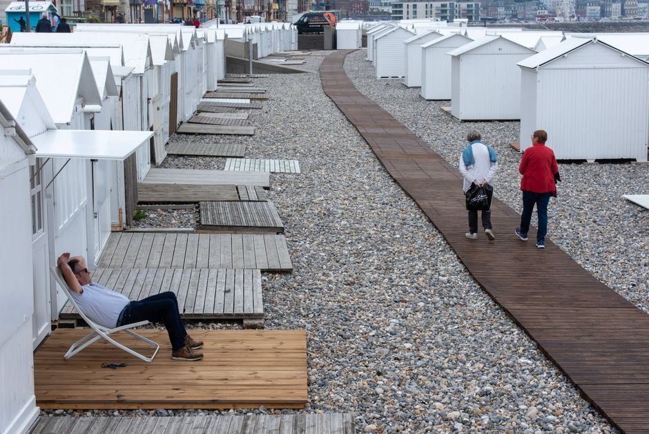 Seaside scene with beach huts and people strolling along the boardwalk in Mers-les-Bains, France.