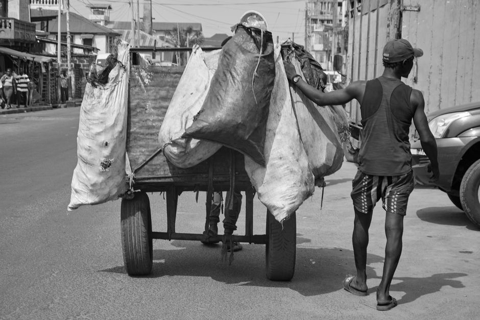 A street vendor in Sierra Leone pushes a cart with goods through an urban street scene.