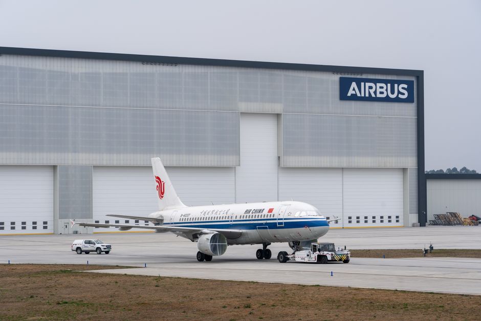 Air China aircraft being towed in front of Airbus hangar.