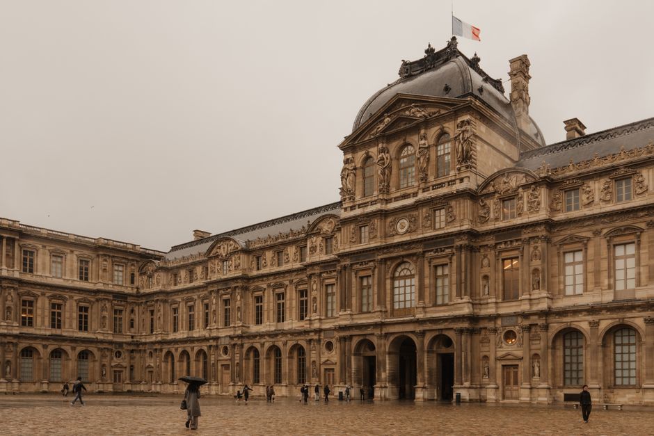 The majestic Louvre Museum courtyard under an overcast sky in Paris, France.
