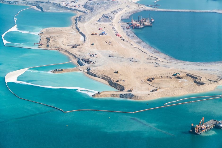 Aerial shot of coastal construction site with vibrant turquoise waters, showcasing land reclamation.