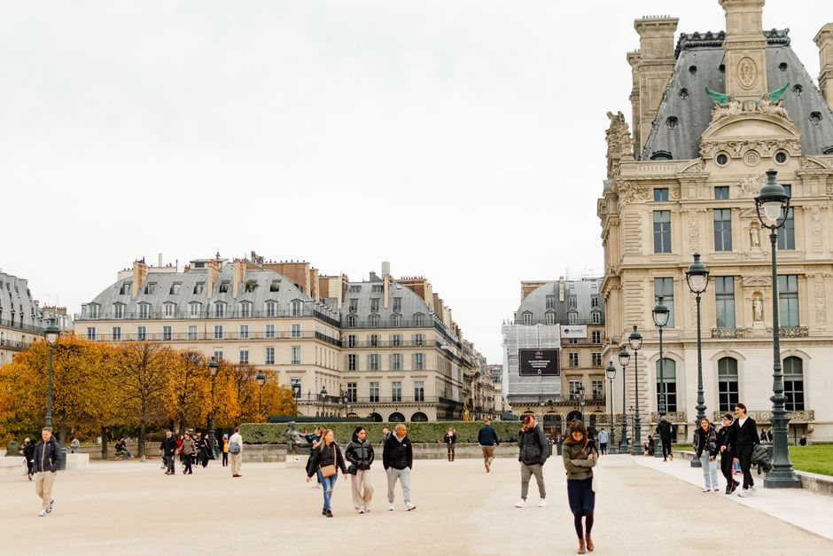 People walking near the historic Louvre Museum in Paris during autumn.