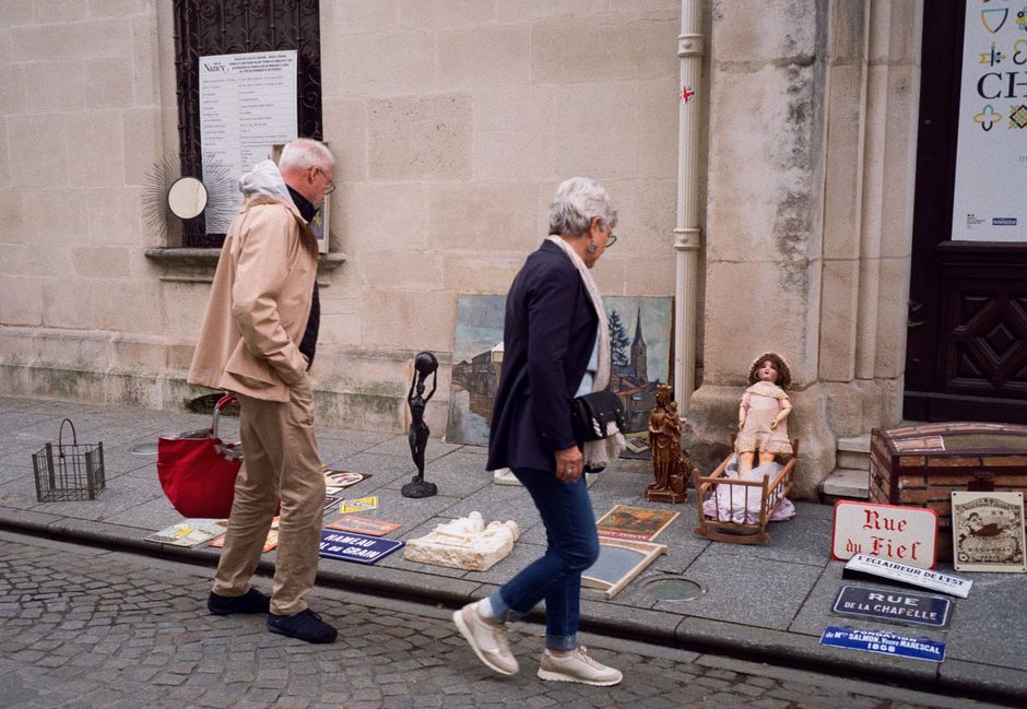 An elderly couple browses a vintage street market in Nancy, France. Historic charm and curiosity come alive.