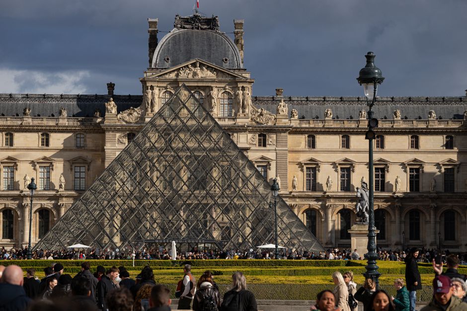 Busy day at the iconic Louvre Pyramid with a crowd of tourists.