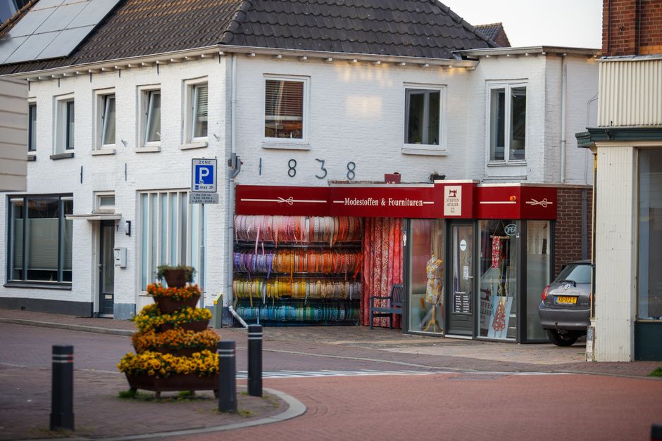 A vibrant textile shop with colorful fabric rolls in a quaint Dutch town street.