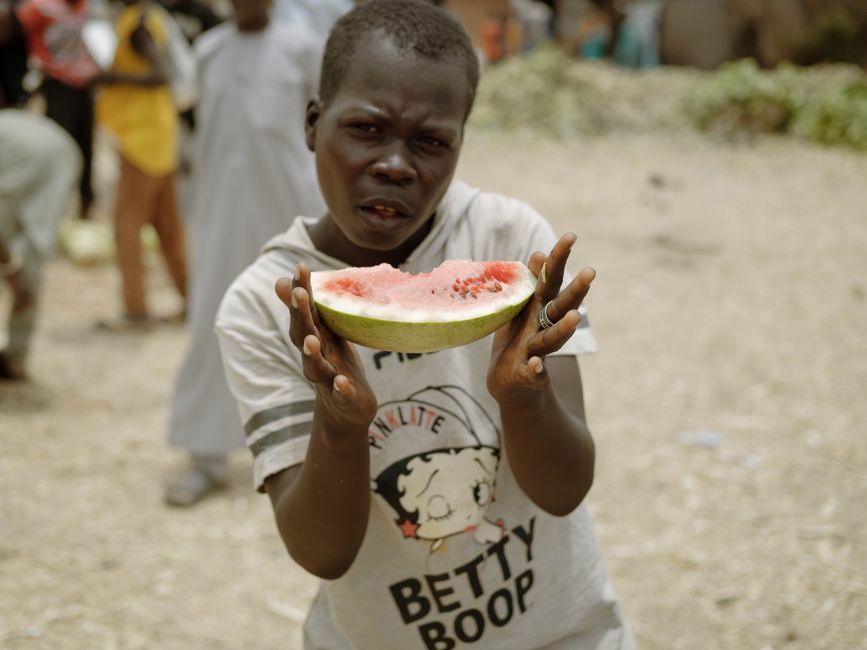Young boy presenting a slice of fresh watermelon outdoors in Zaria, Nigeria.