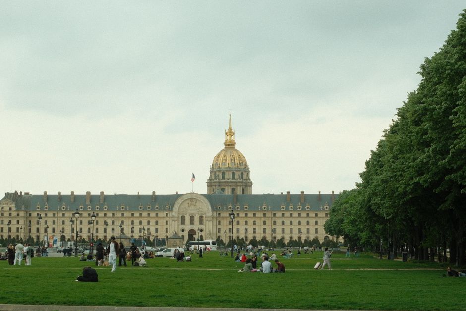 View of Les Invalides in Paris, with people relaxing on the grass under a cloudy sky.