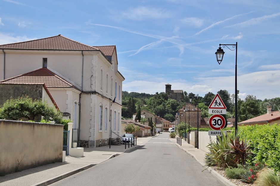 Quaint village street in Chantemerle-les-Blés, France with summer blue skies and lush greenery.