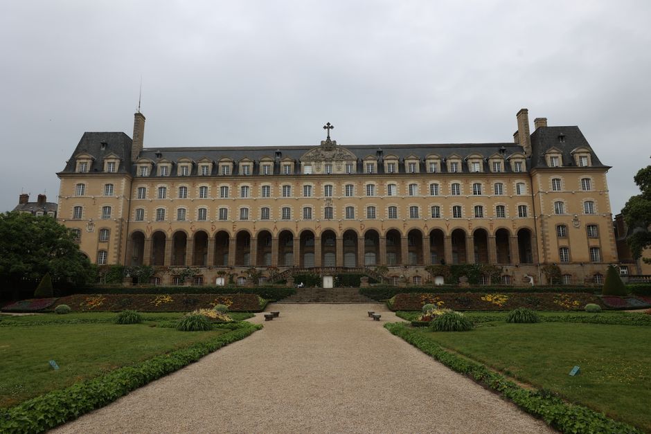Neoclassical building facade with symmetrical garden path on a cloudy day.