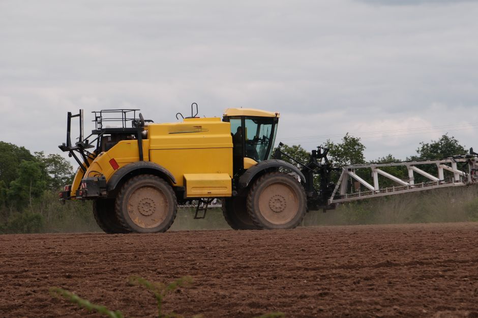 Yellow tractor in a field, used for agricultural work under a cloudy sky.