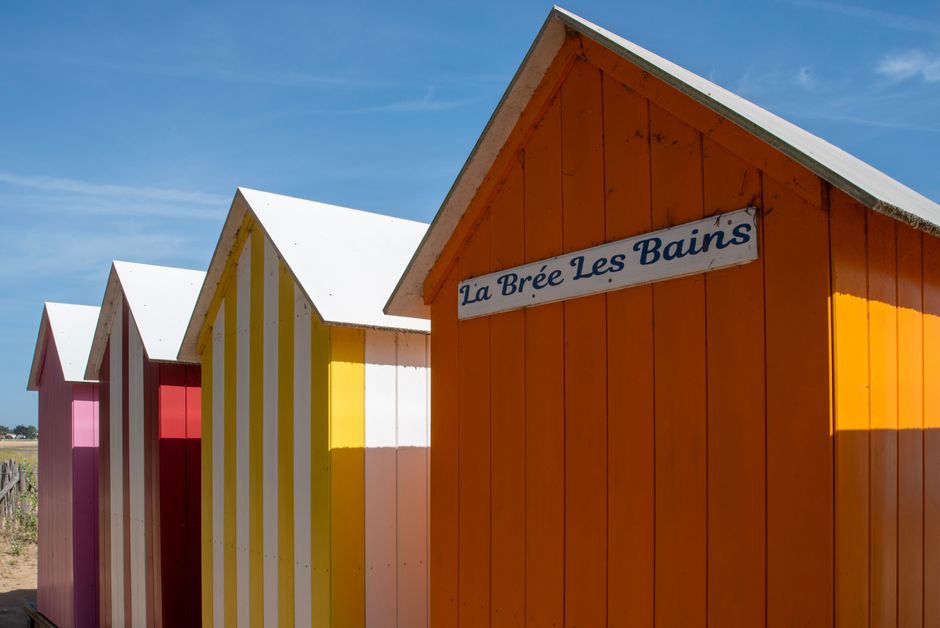 Vibrant striped beach huts in La Brée Les Bains under a clear blue sky.