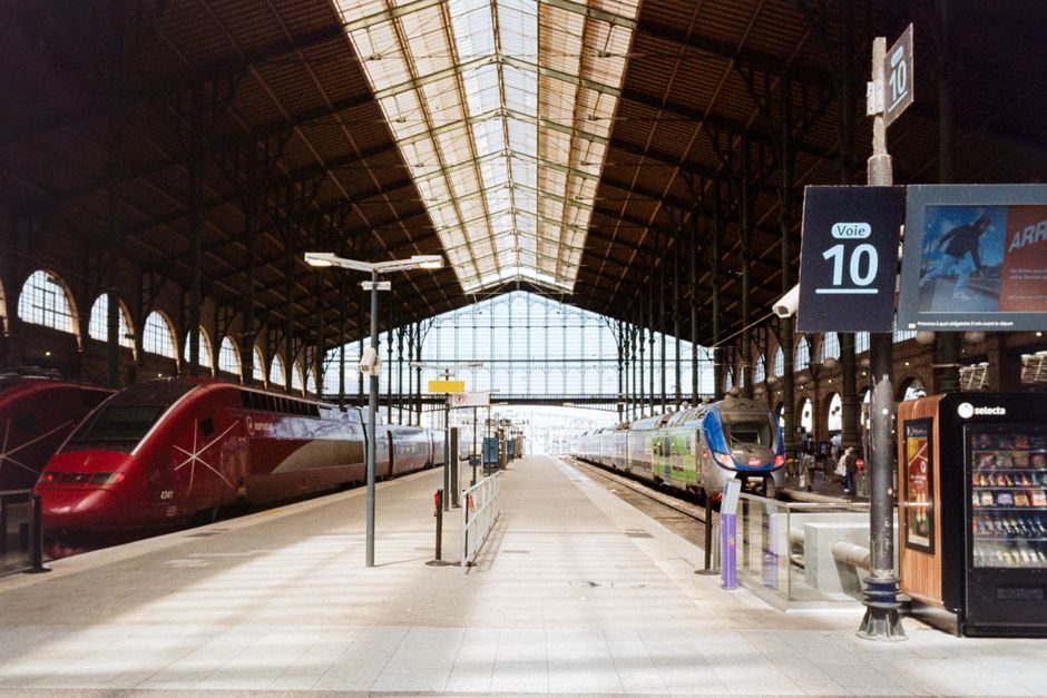 Interior view of Gare du Nord in Paris, showcasing high-speed trains on parallel tracks under the iconic glass roof.