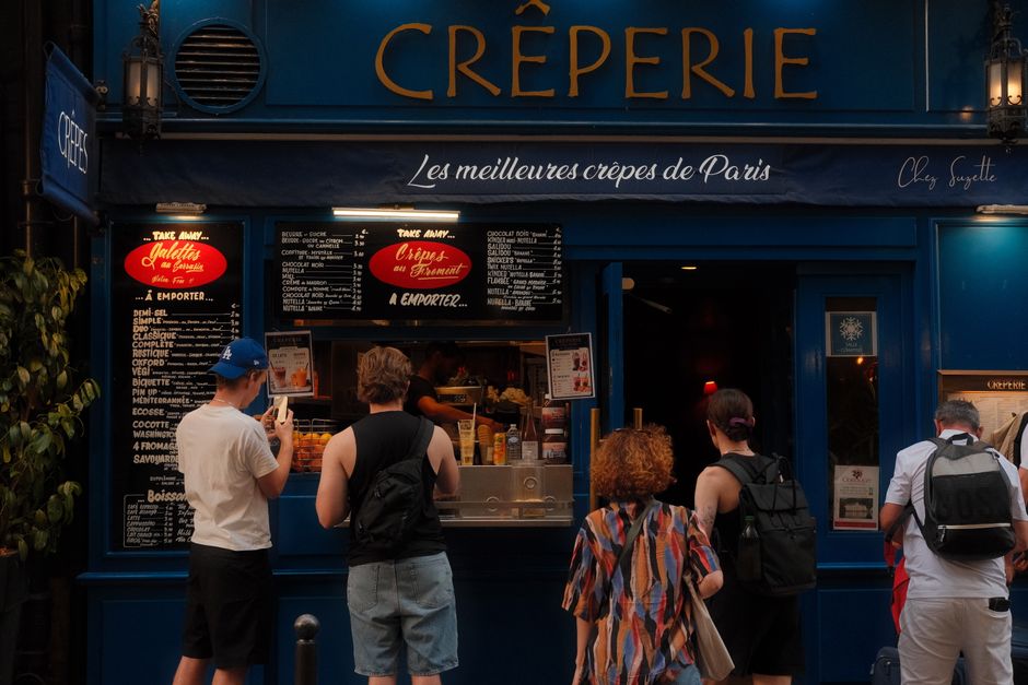 People queuing at a Paris creperie showcasing its inviting blue facade with prominent menu boards.