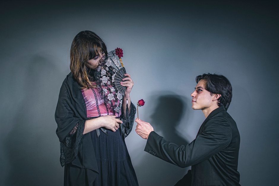 A man kneels offering a rose to a woman holding a decorative fan, creating a romantic scene.