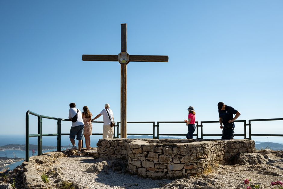 Tourists enjoying the coastal view from a cross-adorned viewpoint in Toulon, France.