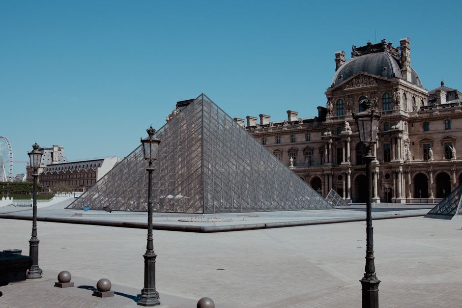 View of the iconic Louvre Pyramid and Museum architecture in Paris under clear blue skies.