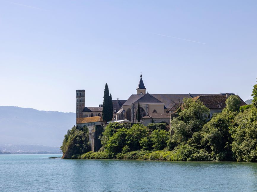 Serene view of a medieval abbey overlooking Lac du Bourget, captured under a clear sky in Auvergne-Rhône-Alpes, France.