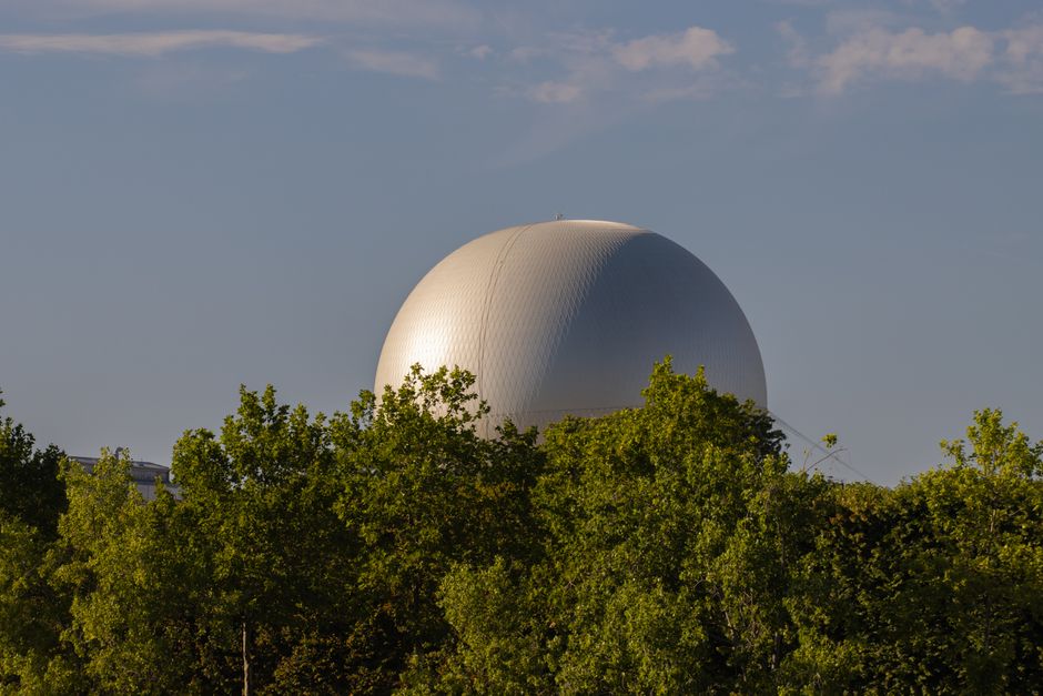 A unique white dome structure peeks above green trees in Paris, creating a striking cityscape view.