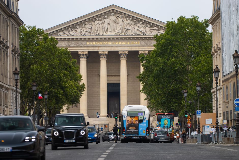 A vibrant Paris street scene with vehicles passing in front of the iconic La Madeleine church.