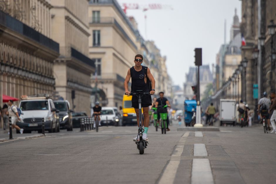 Man rides an electric scooter down a bustling street in Paris, showcasing modern urban transit.