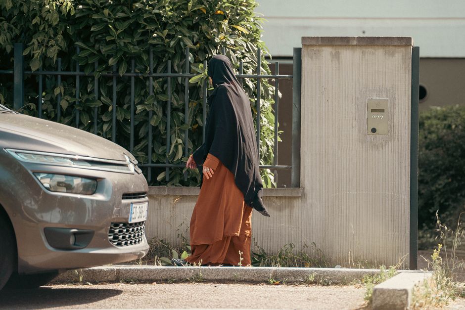 A woman wearing traditional clothing walks along a street beside a parked car.