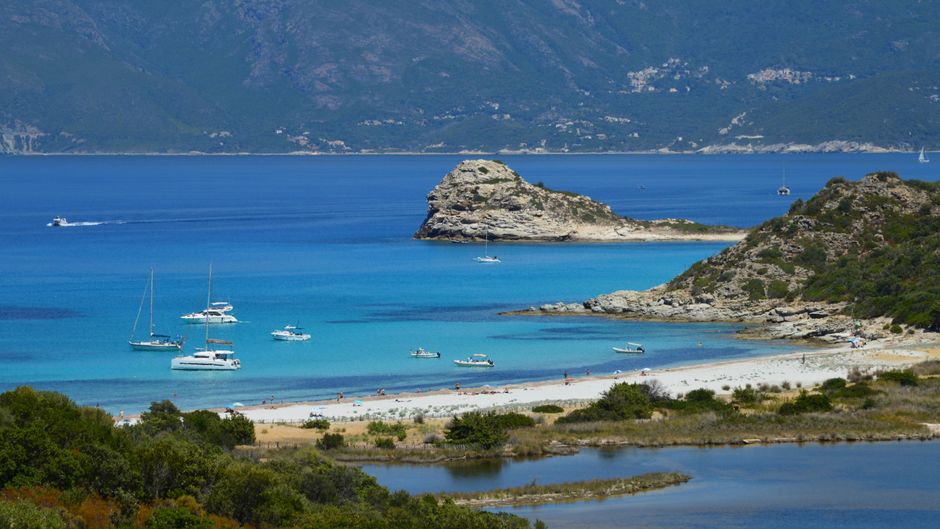 A picturesque coastal scene with boats and a bright beach in Corse, France.