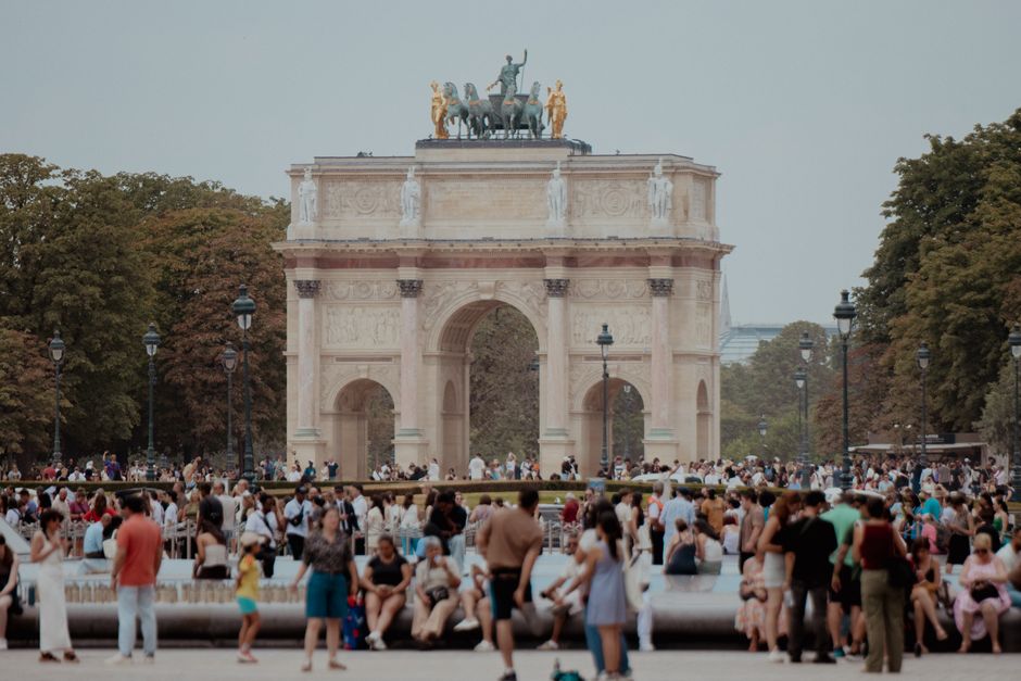 People gather at Arc de Triomphe du Carrousel in Paris, France, during a warm day.