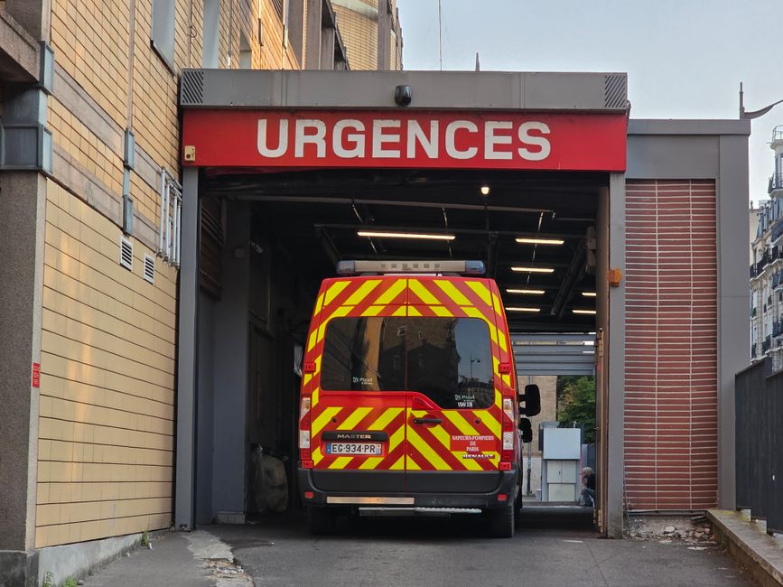 Red and yellow ambulance entering an emergency room at a hospital, marked 'Urgences'.
