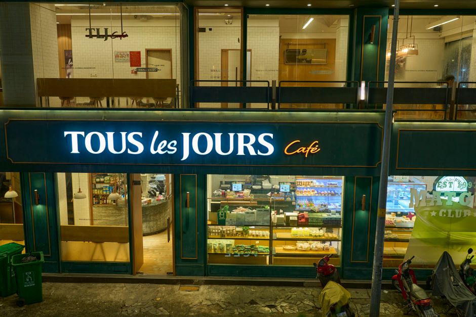 Exterior view of Tous Les Jours Café at night in Ho Chi Minh City showcasing vibrant storefront and interior.