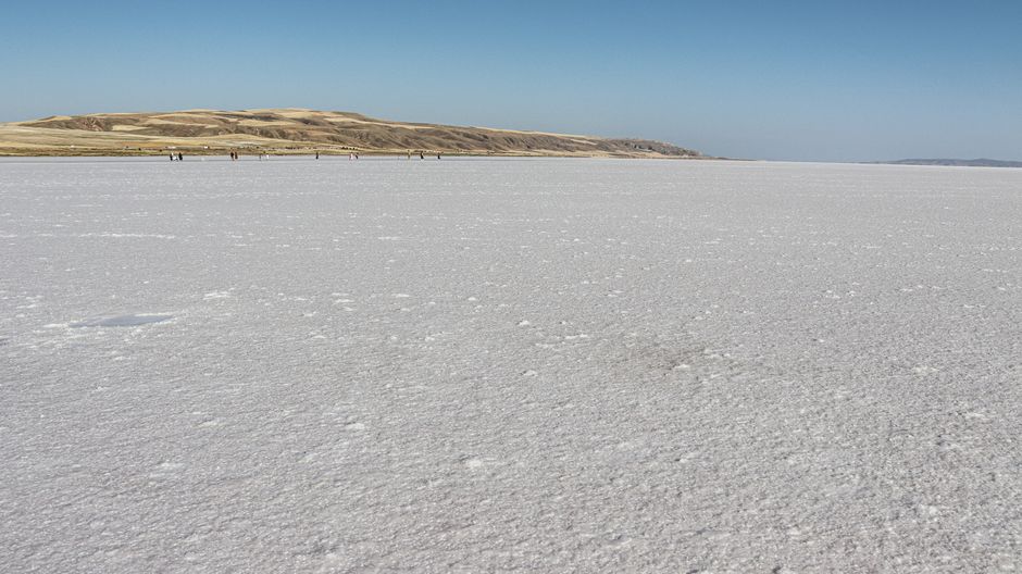 A wide landscape view of the salt flats at Lake Tuz in Ankara, Turkey, under a clear blue sky.