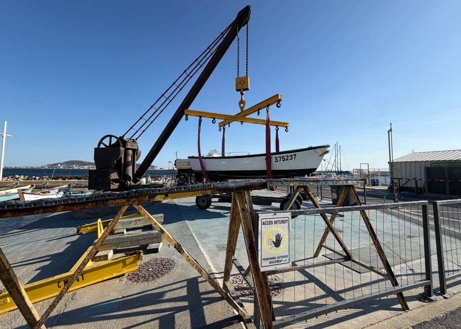 A boat being lifted at a dockyard using a crane on a sunny day.