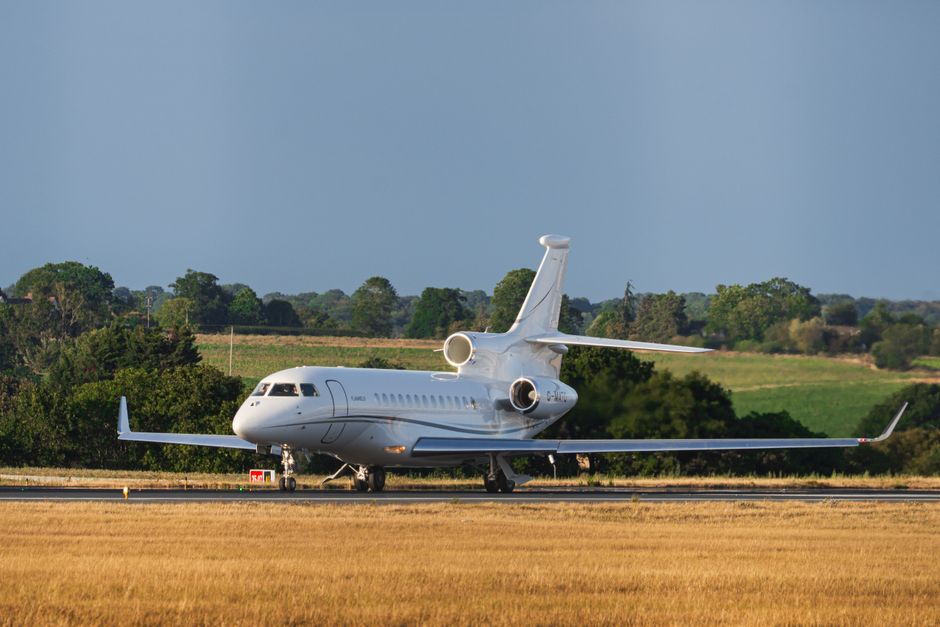 A sleek private jet readies for takeoff on an English runway, surrounded by lush fields.