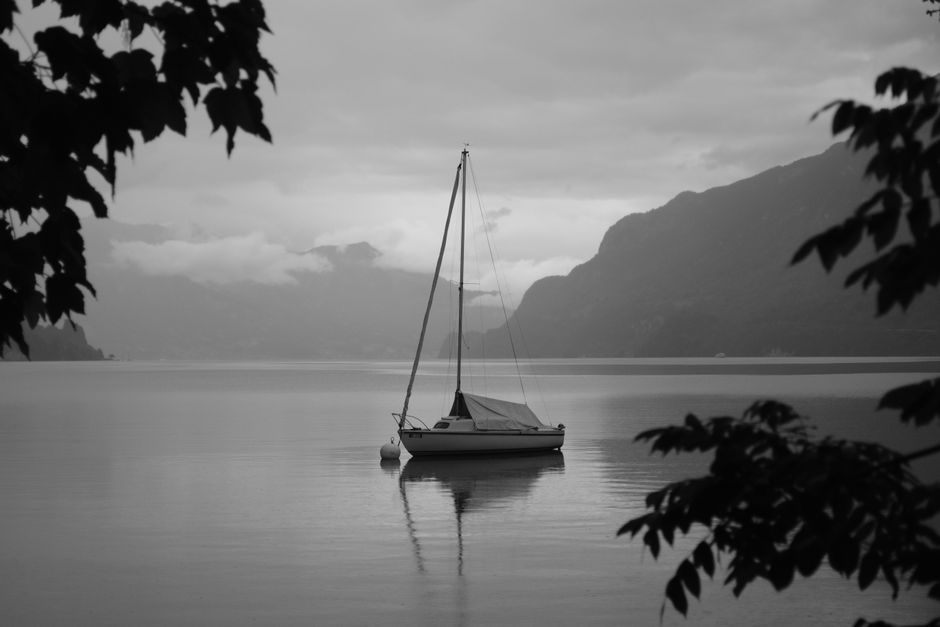 Black and white photo of a sailboat on a tranquil lake in Interlaken, Switzerland.
