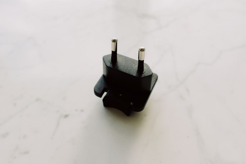 A close-up view of a black electrical adapter on a white marble surface.